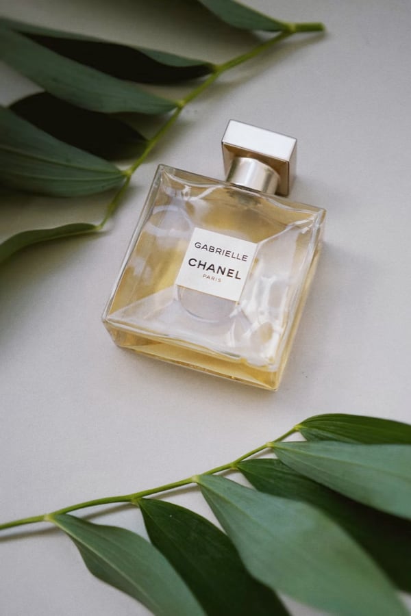 a photo of a perfume bottle on the gray table rounded by some green leaves